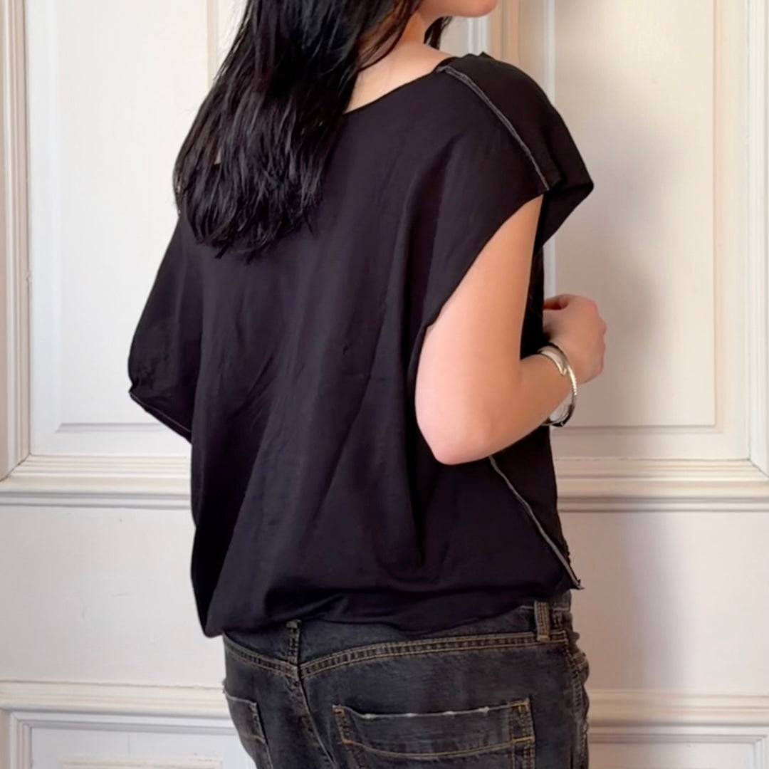 Person wearing a black sleeveless top and dark jeans against a white wall.