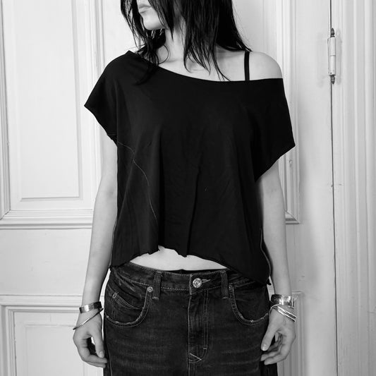 Person wearing a black off-shoulder top and dark jeans against a white wall.