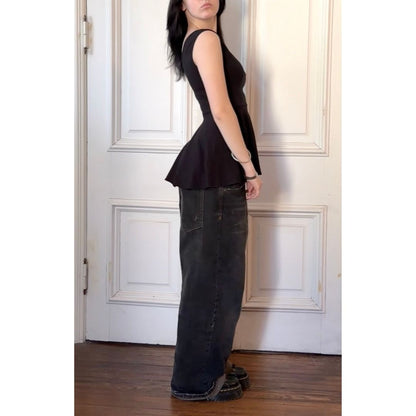 Person wearing a black sleeveless top and dark jeans standing in front of a white paneled door.