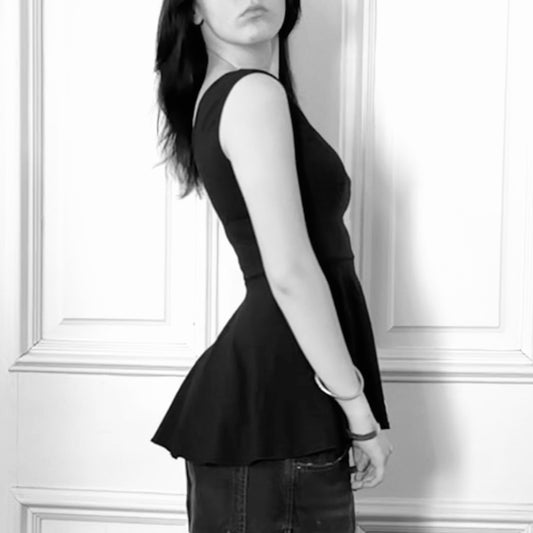 Person wearing a black peplum top against a white paneled wall