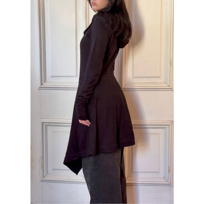 Person wearing a black coat standing against a paneled wall.