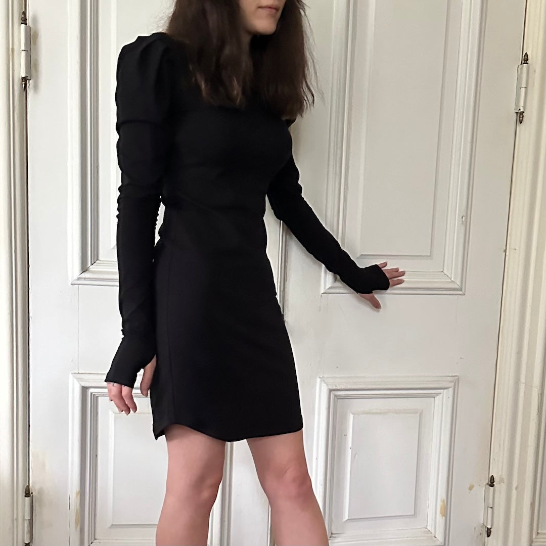 Model wearing La Fae dress, standing beside a door